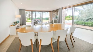Een moderne eetkamer met een ronde houten tafel en witte stoelen, grote ramen met uitzicht op de omgeving, en een accentmuur van natuursteen.