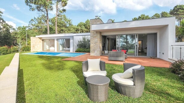 Een modern huis met een zwembad, terras en een verzorgd gazon.