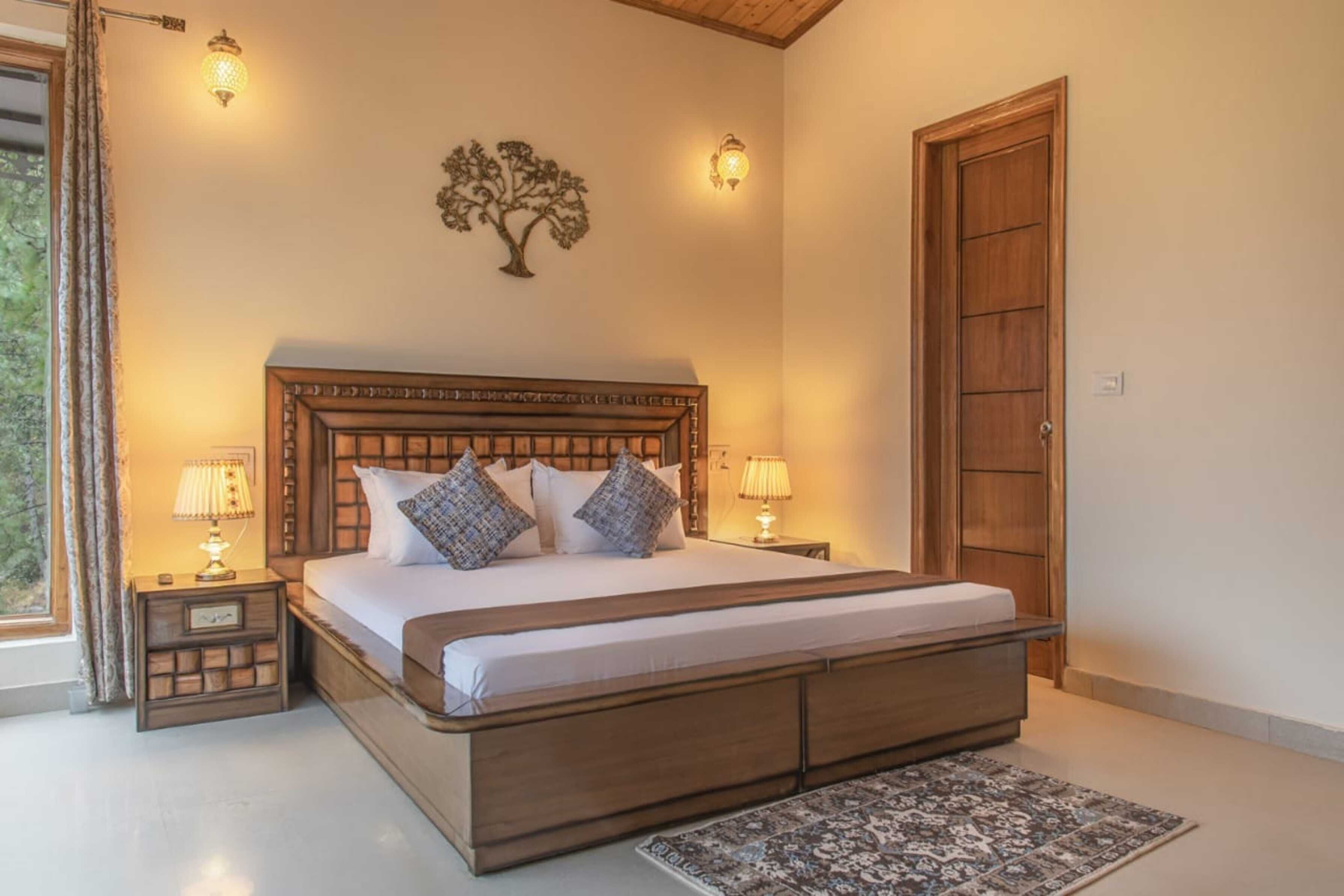 Un dormitorio con una cama grande, dos mesitas de noche con lámparas, un cabecero de madera, un adorno de árbol colgado en la pared y una puerta.