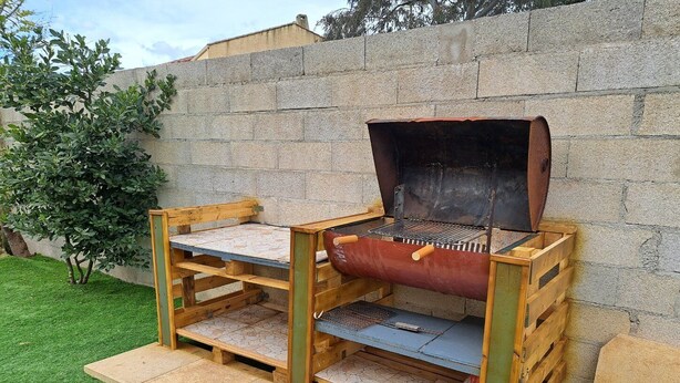 Una parrilla portátil con estructura de madera, rejilla metálica y chimenea.