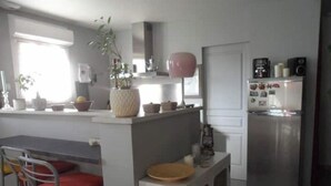 Cocina compacta con refrigerador, cafetera y un pequeño comedor con mesa y sillas.