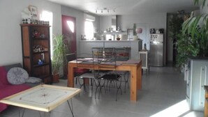 Un amplio espacio de sala con una mesa de comedor, sillas, un sofá y una mesa de centro. Se observa una cocina al fondo con un refrigerador y armarios.