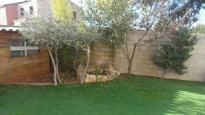 Un jardín bien cuidado con césped artificial, valla de madera y muro de piedra.