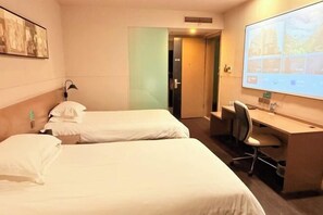 A hotel room with two beds, a desk, a chair, a projector screen, and a door.