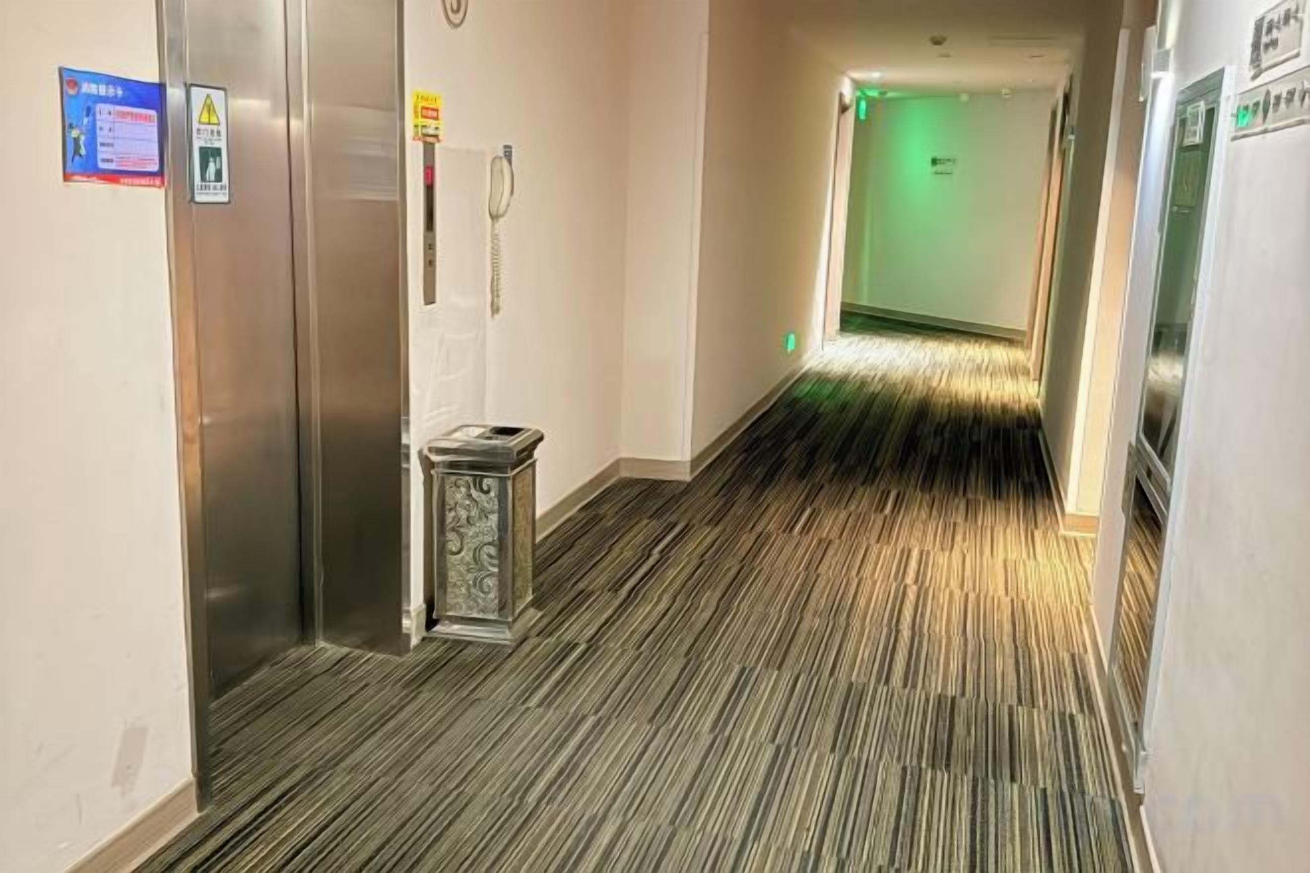 Un pasillo de hotel con alfombra estampada, un bote de basura y una puerta con teléfono.