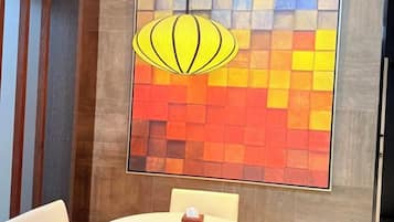 A room with a round table, a hanging light fixture, and a wall with a colorful abstract design.