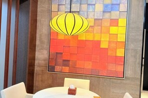 A room with a round table, a hanging light fixture, and a wall with a colorful abstract design.