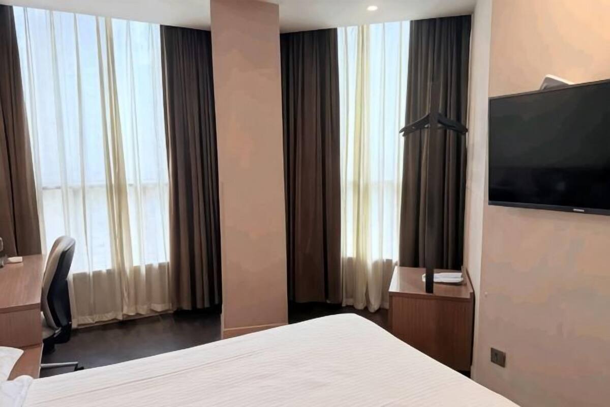 A hotel room with a bed, a desk, a chair, a TV, and a coat rack.