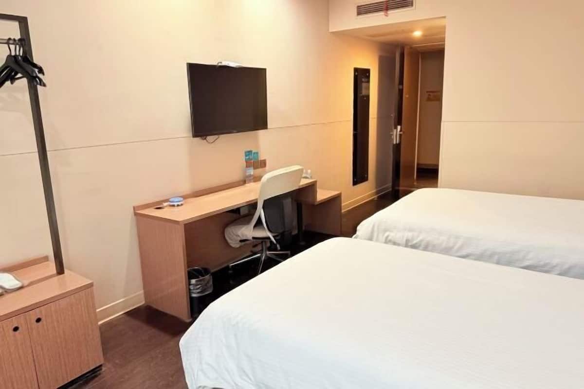 A hotel room with two beds, a desk with a chair, a television mounted on the wall, and a coat rack.