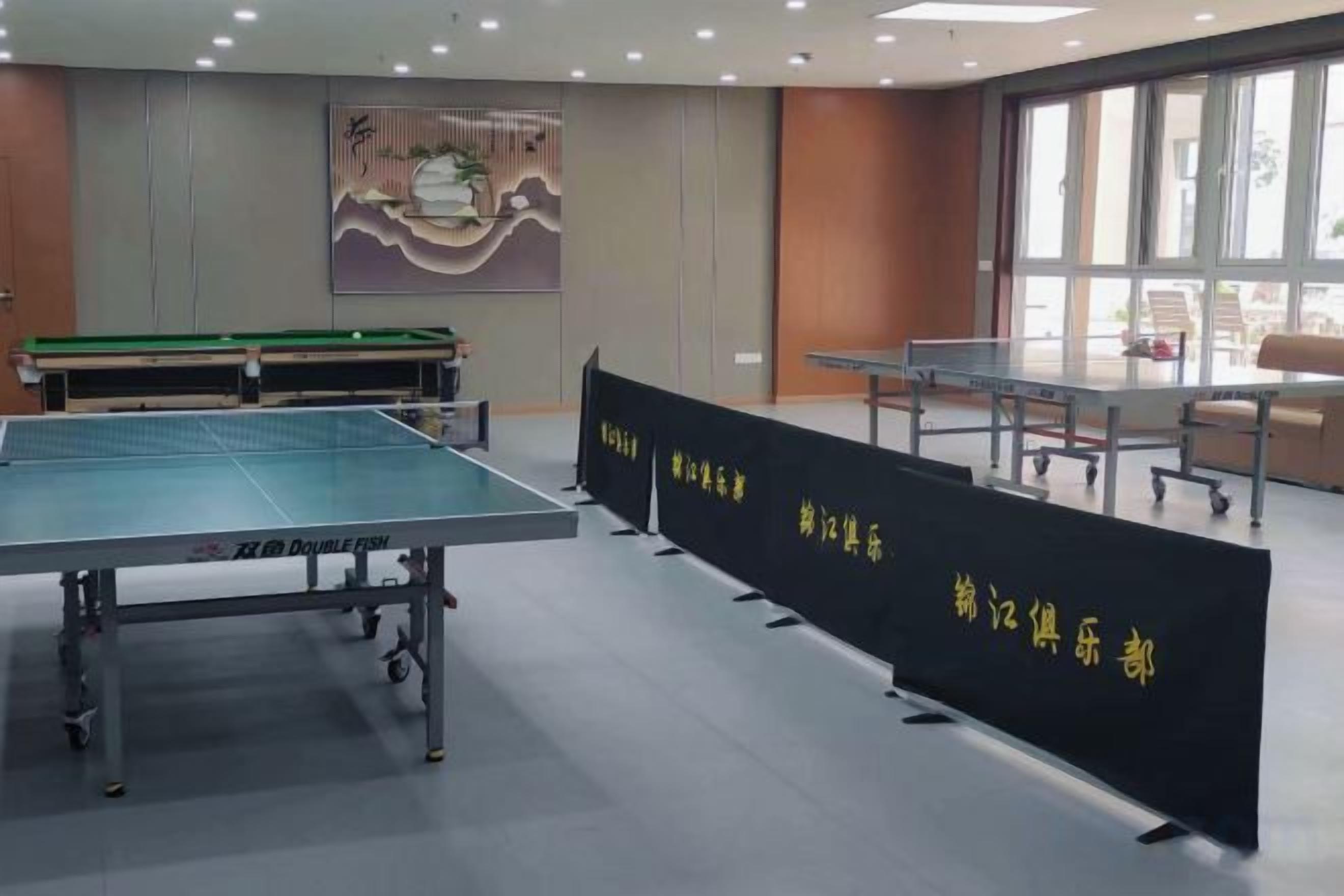 A room with a ping pong table, a billiards table, and a seating area with a view of the outdoors.