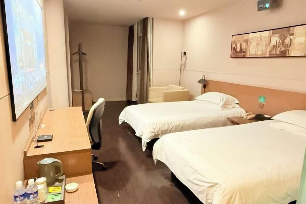 A hotel room with two beds, a desk with a chair, a TV, and a projector screen.