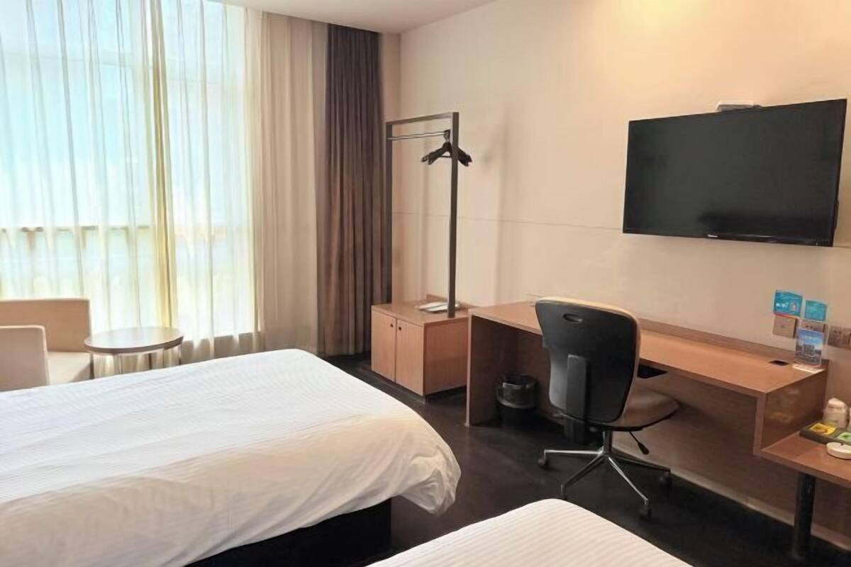 A hotel room with two beds, a desk, a chair, a TV, and a coat rack.
