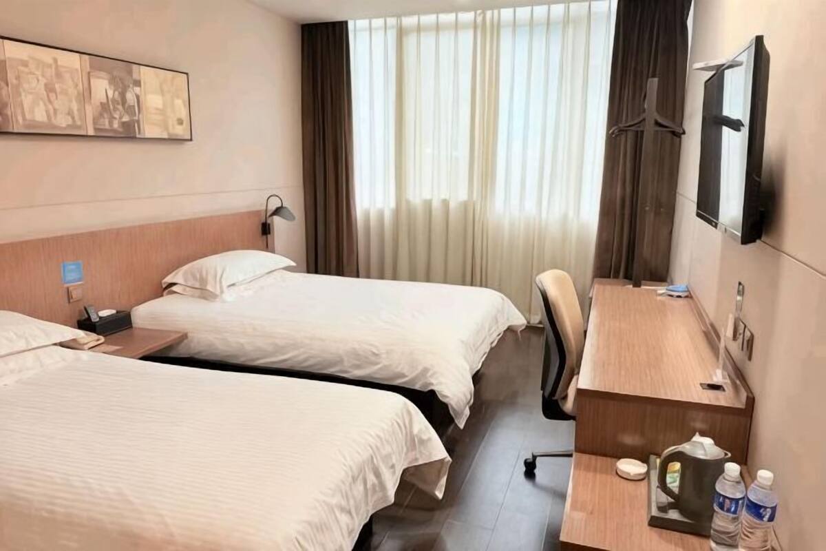 A hotel room with two beds, a desk, a chair, a TV, and a window with curtains.