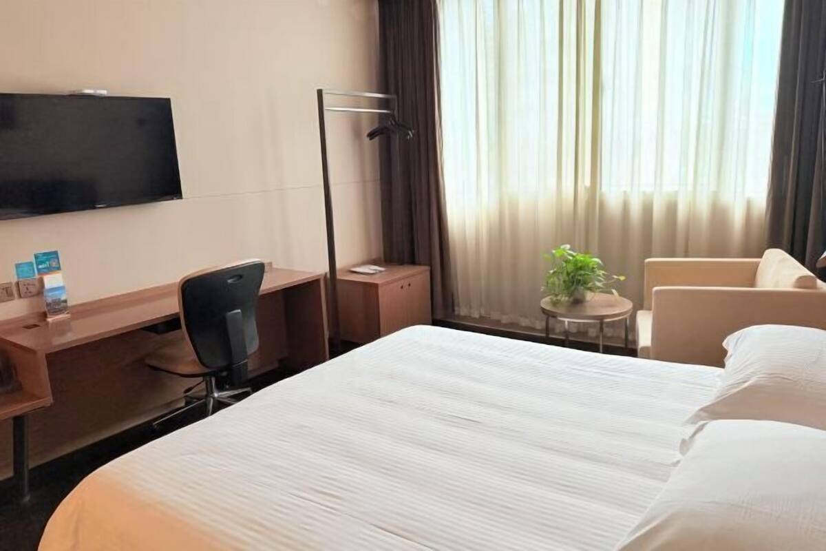 A hotel room with a bed, a desk, a chair, a TV, and a window with curtains.