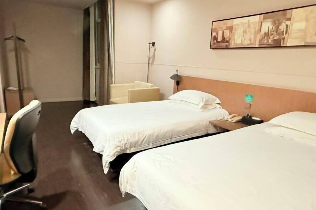 A hotel room with two beds, a desk, a chair, a lamp, and a wall-mounted picture.