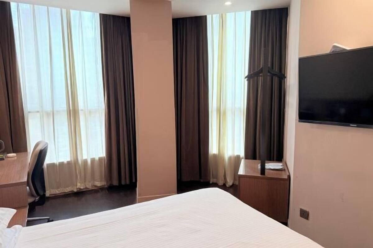 A hotel room with a large bed, a desk, a chair, a TV, and a window with curtains.