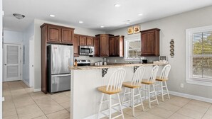 A kitchen with a central island, stainless steel appliances, and white bar stools.
