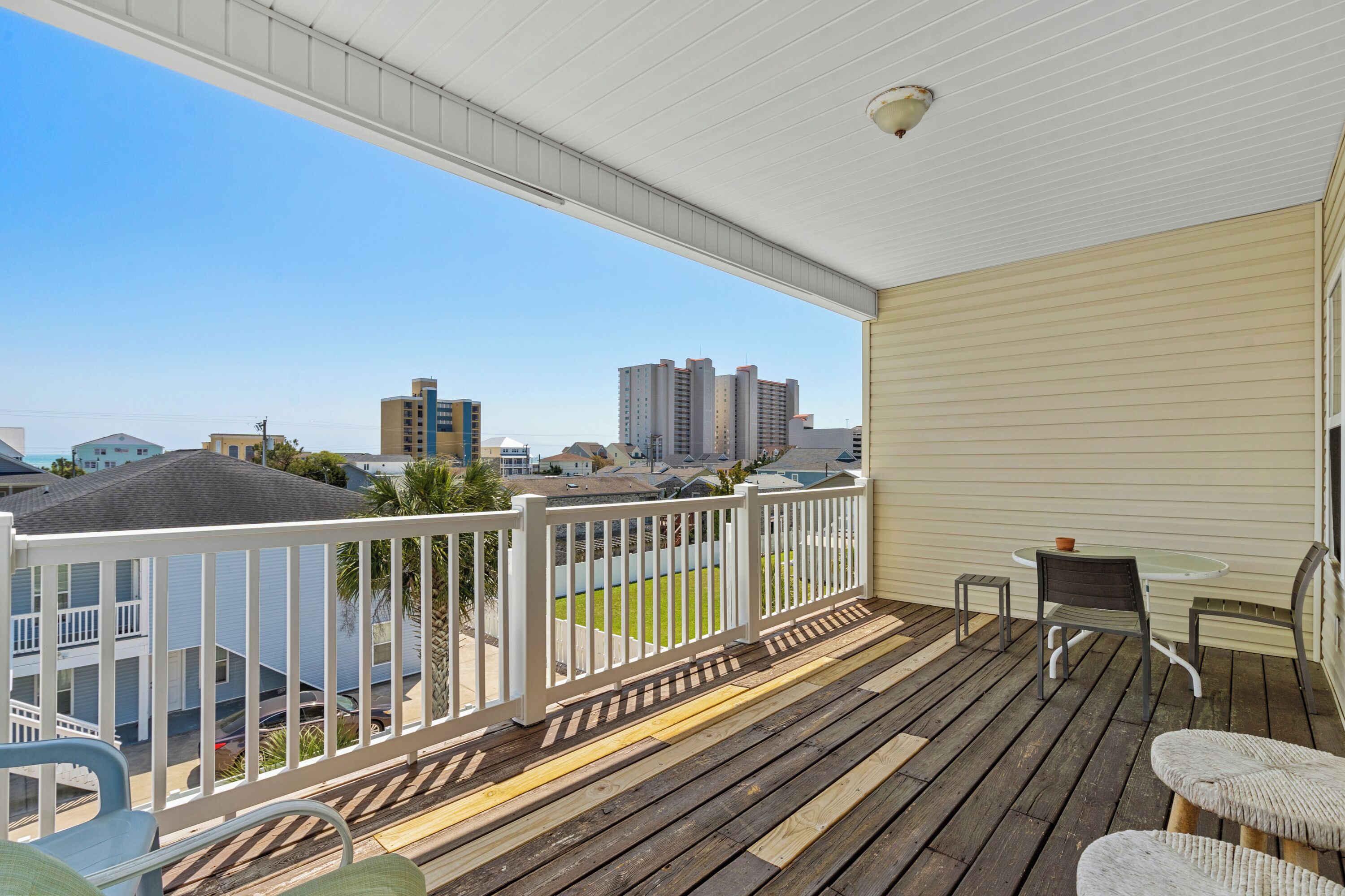 A wooden deck with a white railing, a table, and two chairs.