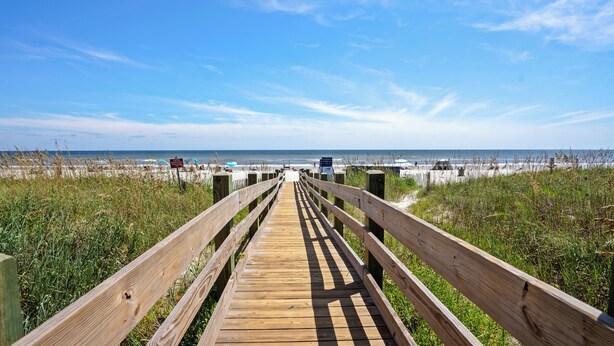 A wooden boardwalk leading to a beach with a clear sky.