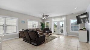 A spacious living room with a leather sofa, a recliner, and a flat-screen TV mounted on the wall.