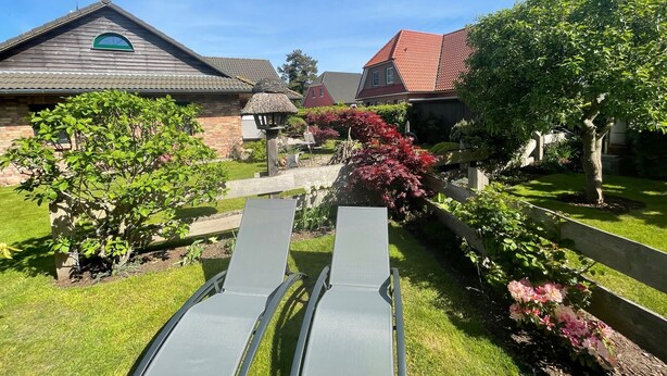 A garden with a wooden fence, a metal bench, and a house with a red roof. - Quietly located vacation apartment with garden (Born a. Darß)