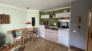 A compact kitchen with white cabinets, a wooden dining table, and a red pendant light. - Quietly located vacation apartment with garden (Born a. Darß)