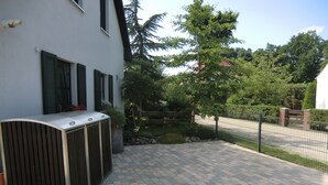 A paved outdoor area with a metal fence, a building with shutters, and a tree. - Quietly located vacation apartment with garden (Born a. Darß)