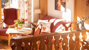 A cozy room with a wooden sofa, a red armchair, a small table with a vase of flowers, and a painting on the wall. - Apartment 9 (Rottach.Apartments) Holiday apartment on Lake Tegernsee (Rottach-Egern)