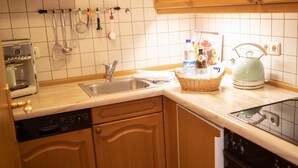 A kitchen with wooden cabinets, a stainless steel sink, a kettle, and various kitchen utensils hanging on the wall. - Apartment 9 (Rottach.Apartments) Holiday apartment on Lake Tegernsee (Rottach-Egern)