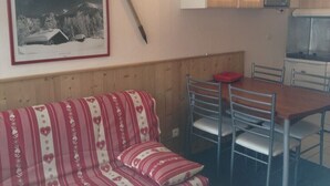 A cozy room with a wooden bench, a dining table with chairs, a framed picture on the wall, and a microwave above the cabinets.