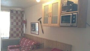 A compact living space with a wooden bench, a small table, and a kitchenette area with a microwave and toaster.