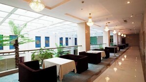 A hotel corridor with a glass ceiling, tables with white tablecloths, dark cushioned seating, and hanging light fixtures. - Keyuan Business Hotel (Jining)