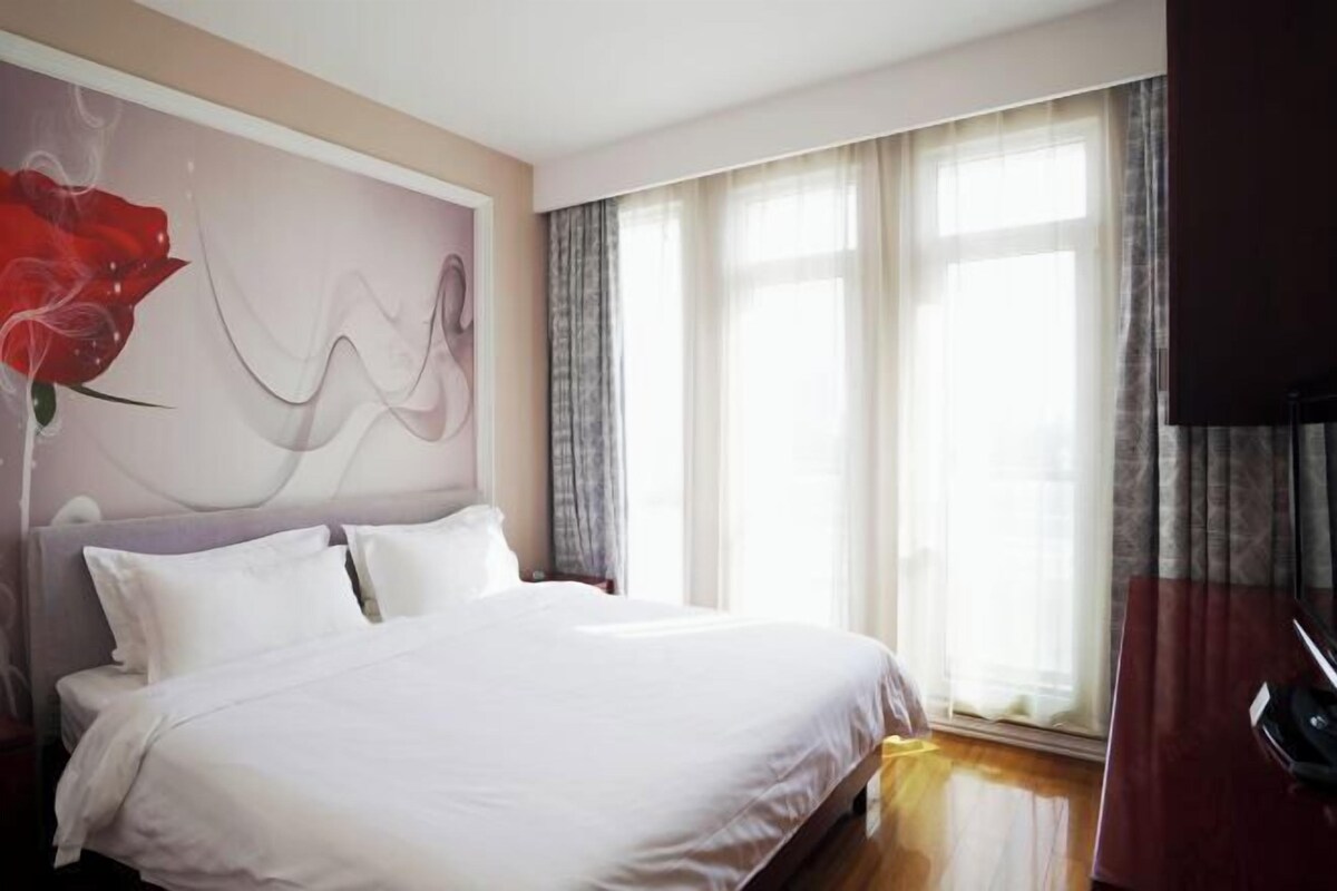 Un dormitorio con cama, un ventanal con cortinas y una pared con diseño floral.