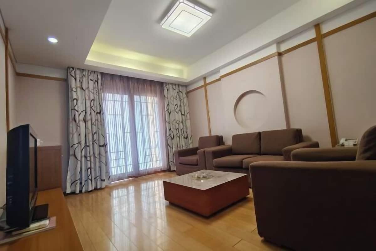 Ein modernes Wohnzimmer mit Flachbildfernseher, zwei Sofas, einem Couchtisch und einem großen Fenster mit Vorhängen.