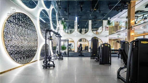A modern gym with various exercise equipment, a large circular mirror, and a unique ceiling design. - Keyuan Business Hotel (Jining)
