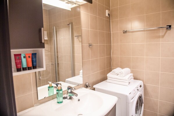 A bathroom with a sink, mirror, and a washing machine. - Origo Leilighetshotell (Drammen)