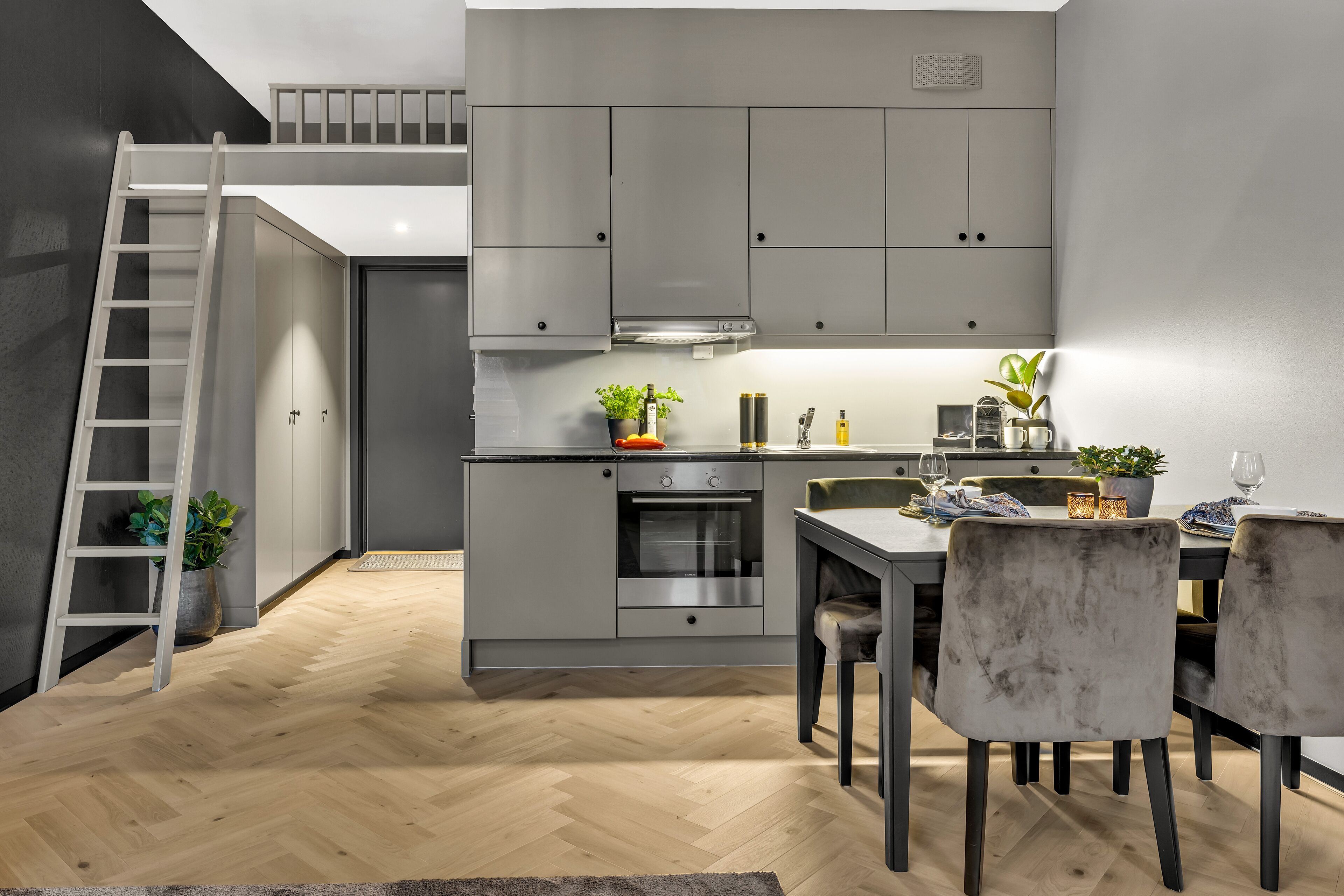 Una cocina moderna con armarios grises, horno empotrado y comedor con mesa y sillas.