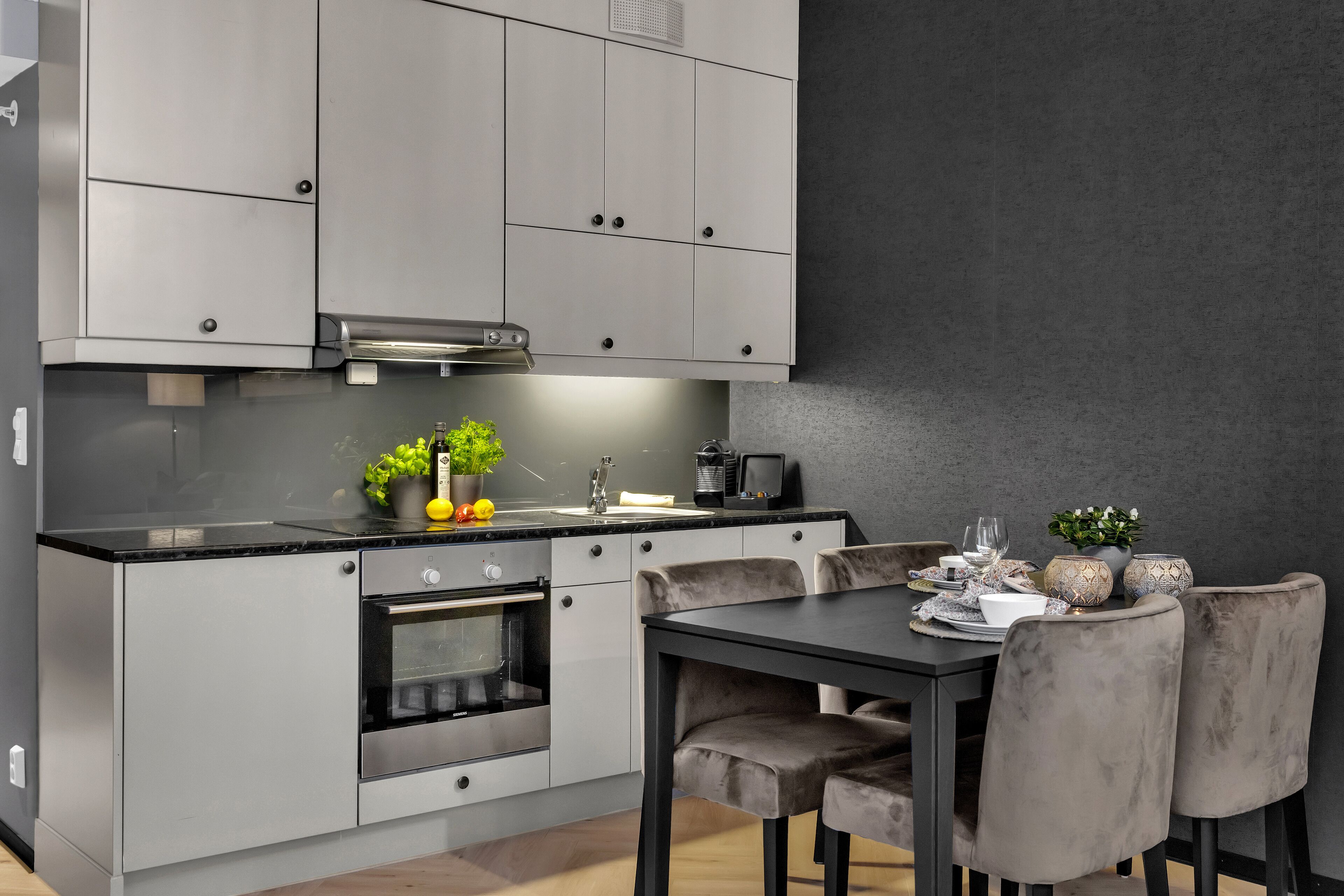 A modern kitchen with grey cabinets, a black countertop, and a dining area with a table and chairs.