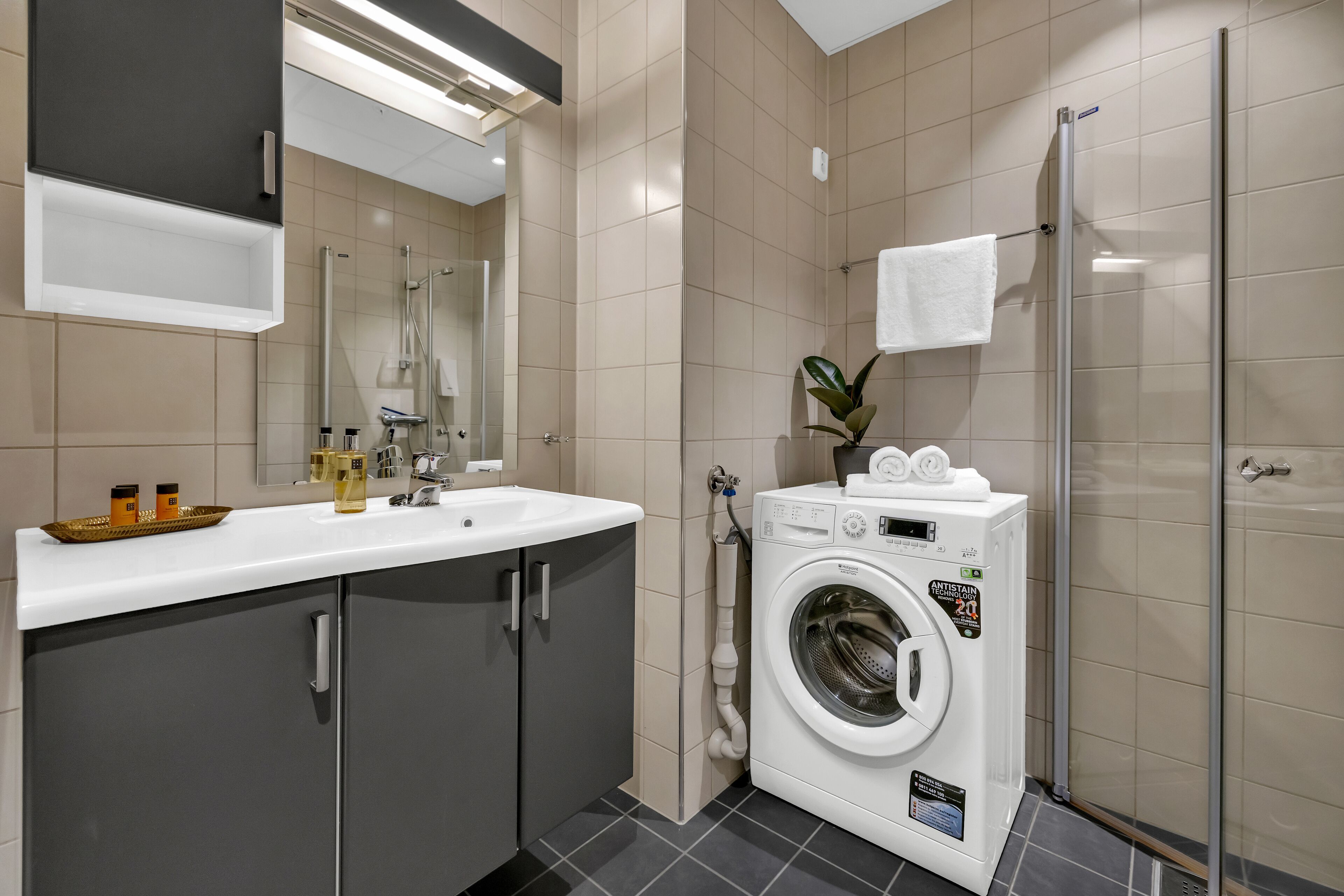 Ein modernes Badezimmer mit Waschbecken, Spiegel, Waschmaschine und Dusche.