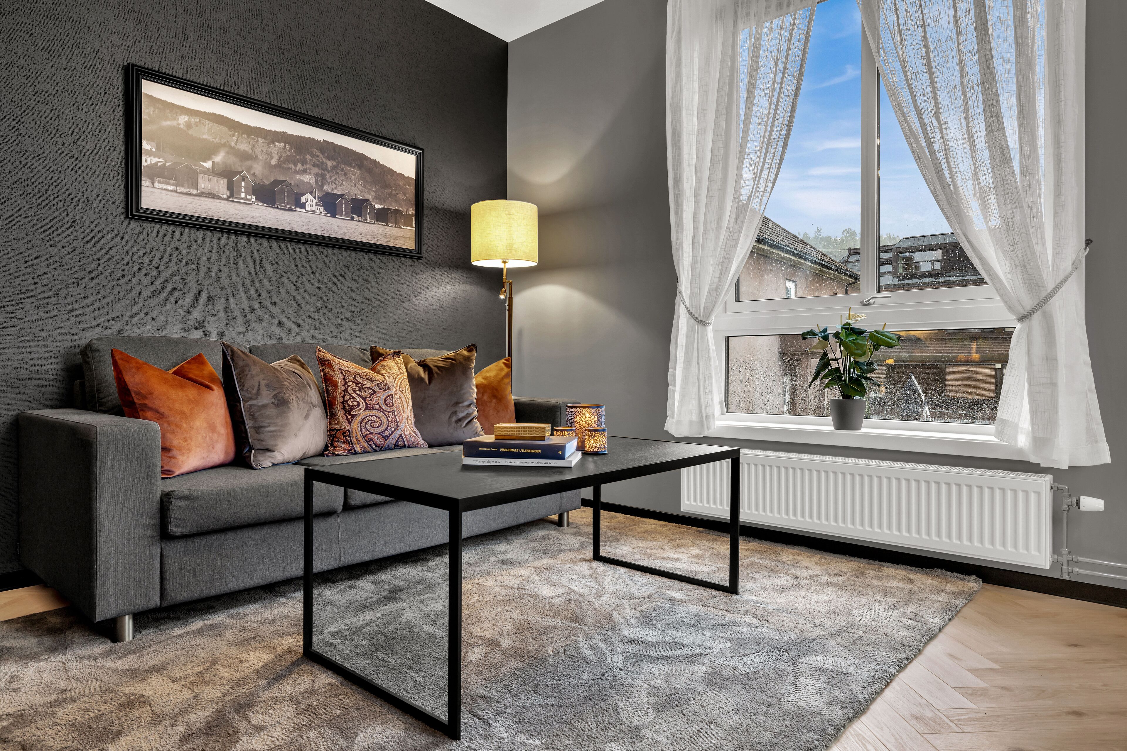 Una sala de estar moderna con un sofá gris, una mesa de centro negra y un ventanal con cortinas blancas.