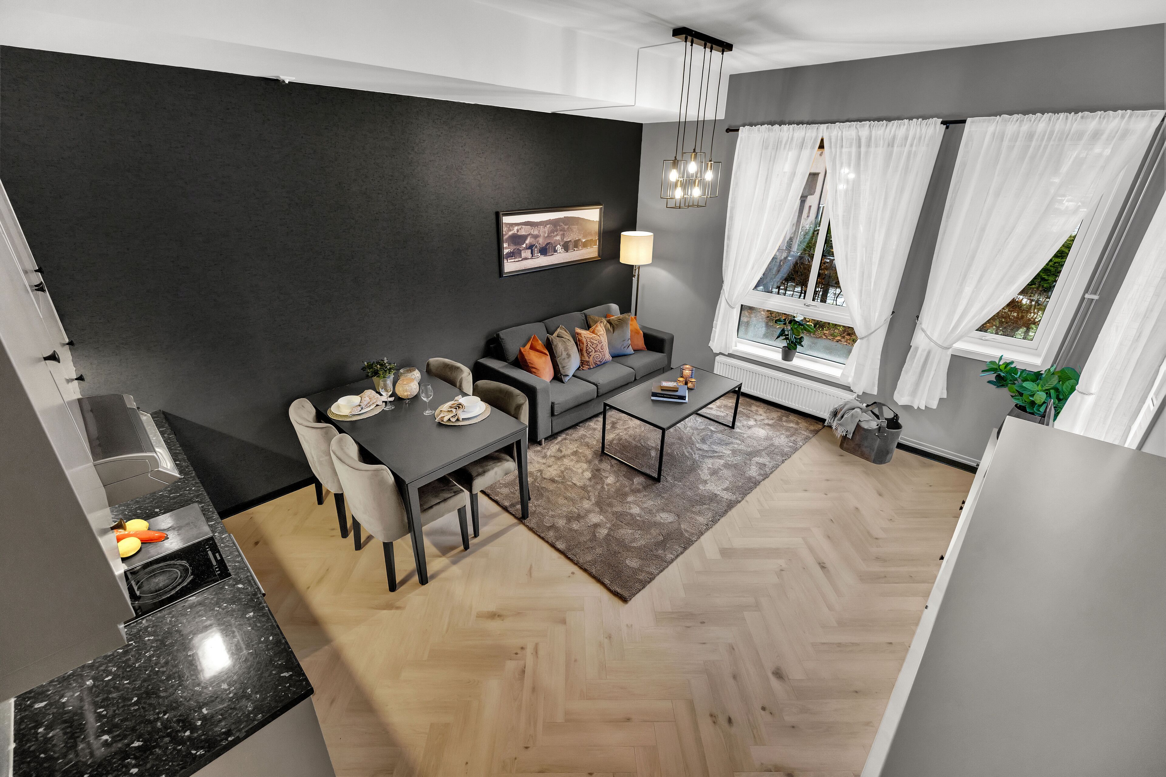 Una sala de estar moderna con un sofá gris, una mesa de comedor y un piso de madera en espiga.