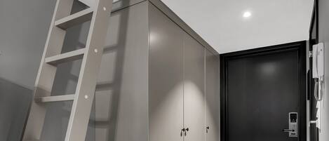 A modern interior with a wooden floor, a black door, and a white ladder against a grey wall.