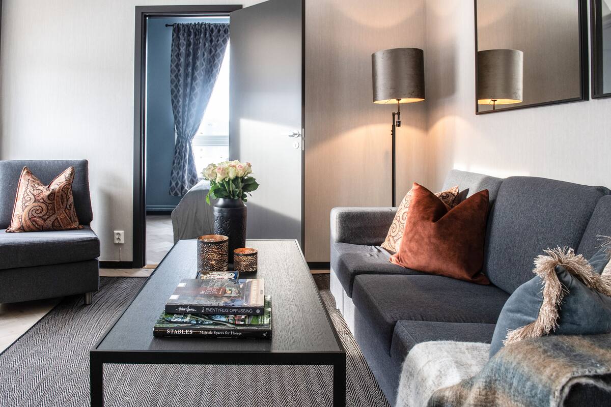 Un salon moderne avec un canapé gris, une table basse sur laquelle sont posés des livres, un vase rempli de fleurs et une lampe.