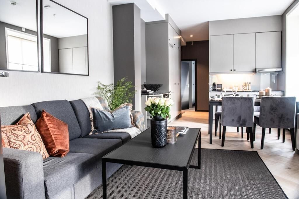 Ein modernes Wohnzimmer mit einem grauen Sofa, einem schwarzen Couchtisch und einem Essbereich mit grauen Stühlen.