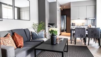 Ein modernes Wohnzimmer mit einem grauen Sofa, einem schwarzen Couchtisch und einem Essbereich mit grauen Stühlen.