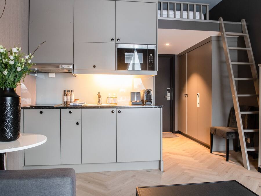 A modern kitchen with white cabinets, a stainless steel microwave, and a small island. There is a vase with flowers on a table, and a ladder leaning against the wall.