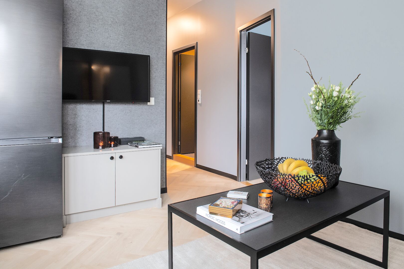 Una cocina moderna con televisor de pantalla plana, un armario blanco y una zona de comedor con mesa negra.
