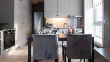 A modern kitchen with white cabinets, a built-in oven, and a dining area with two grey upholstered chairs.