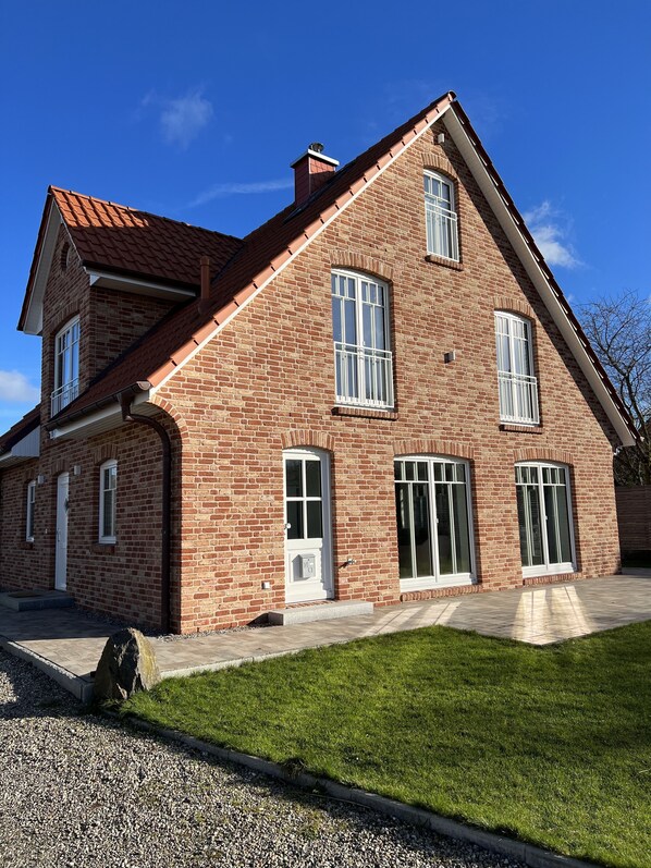 A two-story brick house with a red-tiled roof, large windows, and a well-maintained lawn.