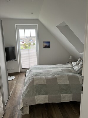 A bedroom with a bed, a TV, a door leading outside, and a small picture on the wall.